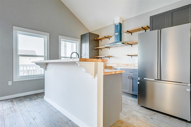 kitchen featuring vaulted ceiling, island range hood, a kitchen bar, light hardwood / wood-style flooring, and stainless steel fridge