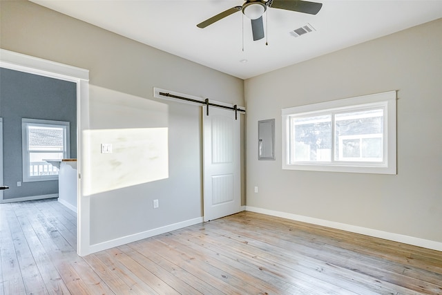 unfurnished bedroom with a barn door, light hardwood / wood-style floors, and ceiling fan