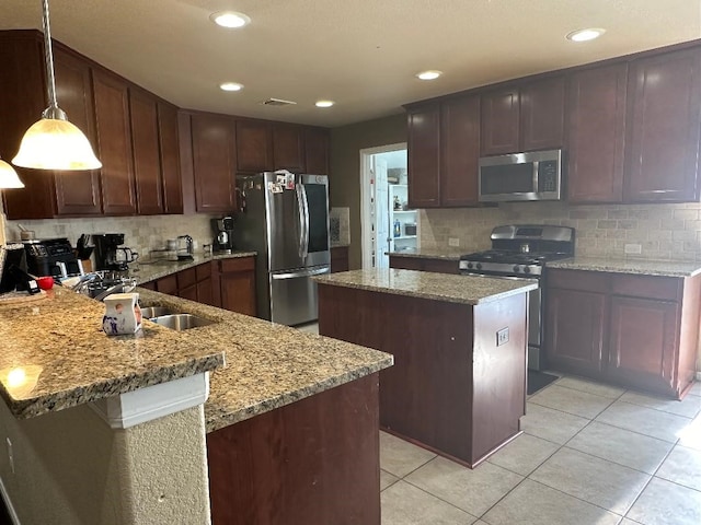 kitchen with light stone counters, a kitchen island, decorative light fixtures, backsplash, and appliances with stainless steel finishes