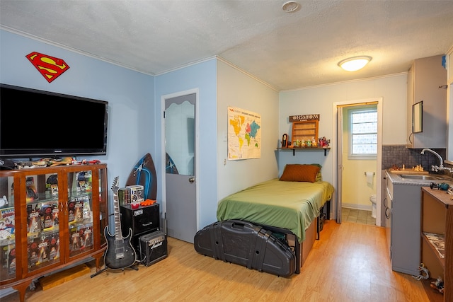 bedroom featuring connected bathroom, ornamental molding, sink, a textured ceiling, and light hardwood / wood-style floors