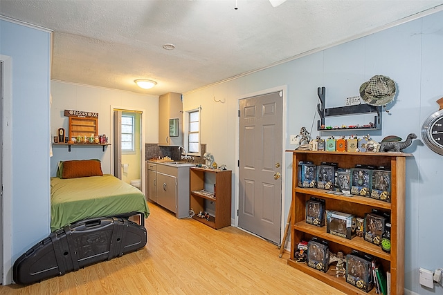 bedroom with a textured ceiling, light hardwood / wood-style floors, sink, and crown molding