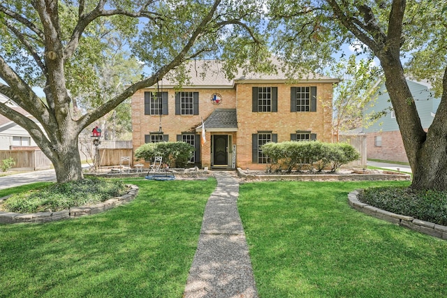 view of front facade featuring brick siding, a shingled roof, fence, and a front yard