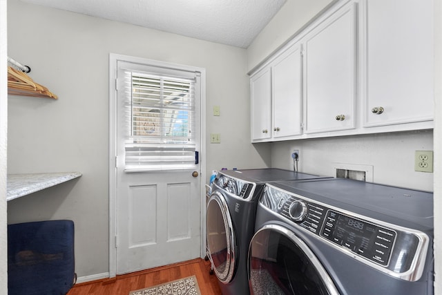 laundry room featuring washing machine and clothes dryer, a textured ceiling, cabinets, and dark wood-type flooring