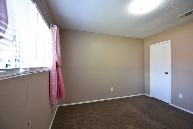 unfurnished room with dark colored carpet and a textured ceiling