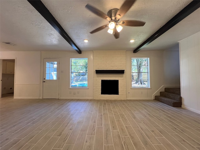 unfurnished living room featuring beamed ceiling, light hardwood / wood-style floors, a textured ceiling, and a brick fireplace