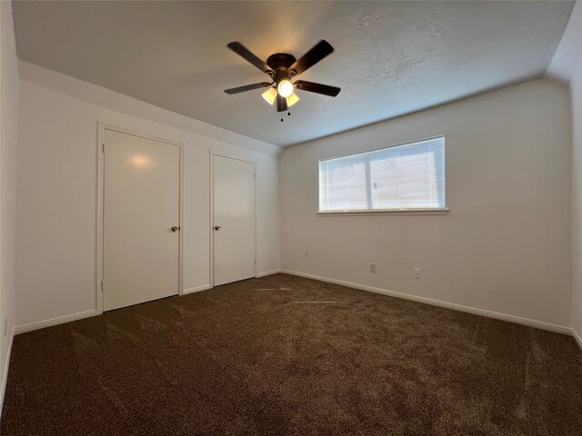 unfurnished bedroom with a textured ceiling, ceiling fan, vaulted ceiling, and dark colored carpet