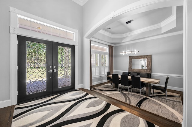 foyer with a raised ceiling, ornamental molding, french doors, a chandelier, and hardwood / wood-style floors