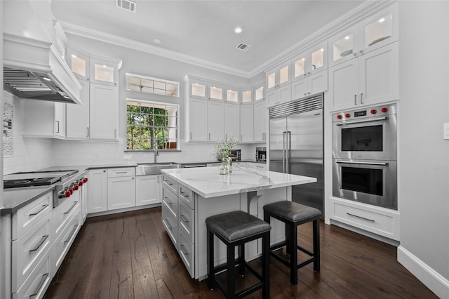 kitchen featuring white cabinets, appliances with stainless steel finishes, custom range hood, a center island, and a kitchen bar