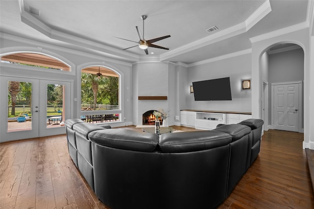 living room with dark wood-type flooring, a fireplace, a raised ceiling, ornamental molding, and ceiling fan