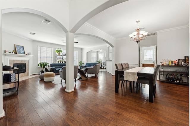 dining area featuring ornamental molding, ceiling fan with notable chandelier, dark wood-type flooring, and a tile fireplace