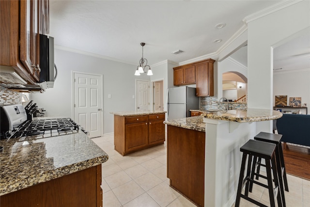 kitchen featuring appliances with stainless steel finishes, decorative backsplash, light stone countertops, pendant lighting, and ornamental molding