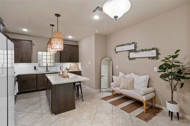 kitchen featuring pendant lighting, sink, dark brown cabinets, a kitchen island, and decorative backsplash