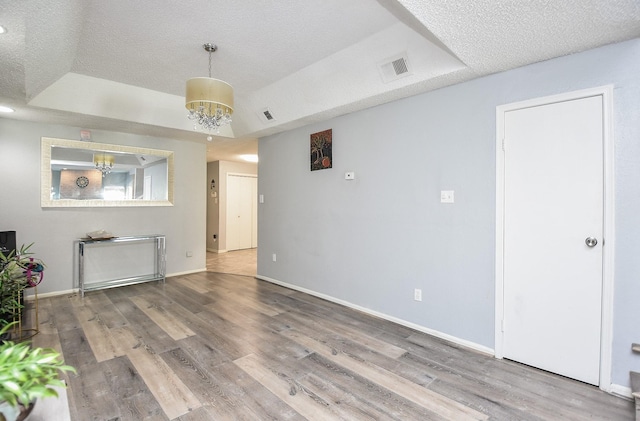 unfurnished living room featuring a textured ceiling, hardwood / wood-style flooring, an inviting chandelier, and a tray ceiling