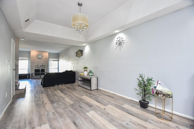 living room with a textured ceiling, a tray ceiling, wood-type flooring, a notable chandelier, and a fireplace