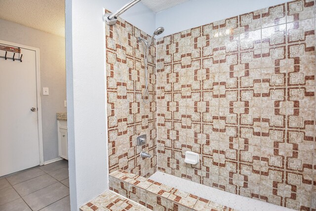 bathroom with tile patterned flooring, a tile shower, a textured ceiling, and vanity