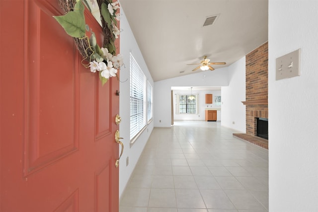 foyer entrance featuring light tile patterned flooring, vaulted ceiling, ceiling fan, and a brick fireplace