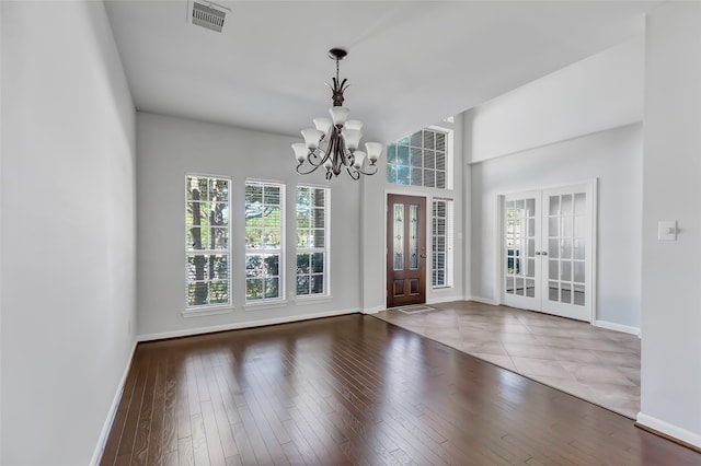 unfurnished dining area featuring french doors, dark wood-type flooring, a chandelier, and a healthy amount of sunlight