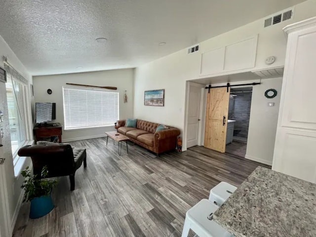 living room featuring vaulted ceiling, hardwood / wood-style flooring, a barn door, and a textured ceiling