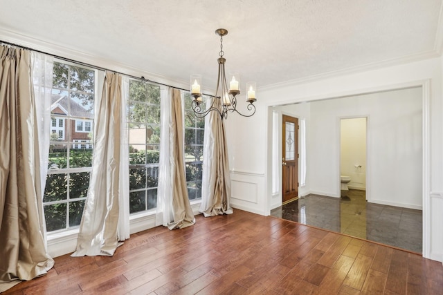 unfurnished dining area featuring dark hardwood / wood-style floors, ornamental molding, a textured ceiling, and an inviting chandelier