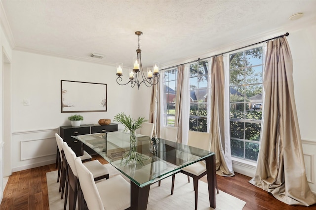 dining room with an inviting chandelier, dark wood-type flooring, a textured ceiling, and ornamental molding