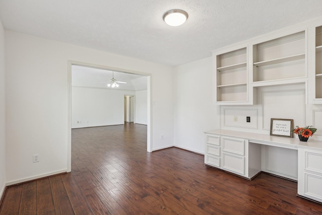 unfurnished office featuring a textured ceiling, built in desk, ceiling fan, and dark wood-type flooring