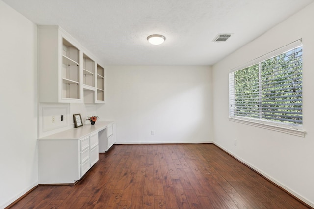 interior space with a textured ceiling, built in desk, and dark wood-type flooring