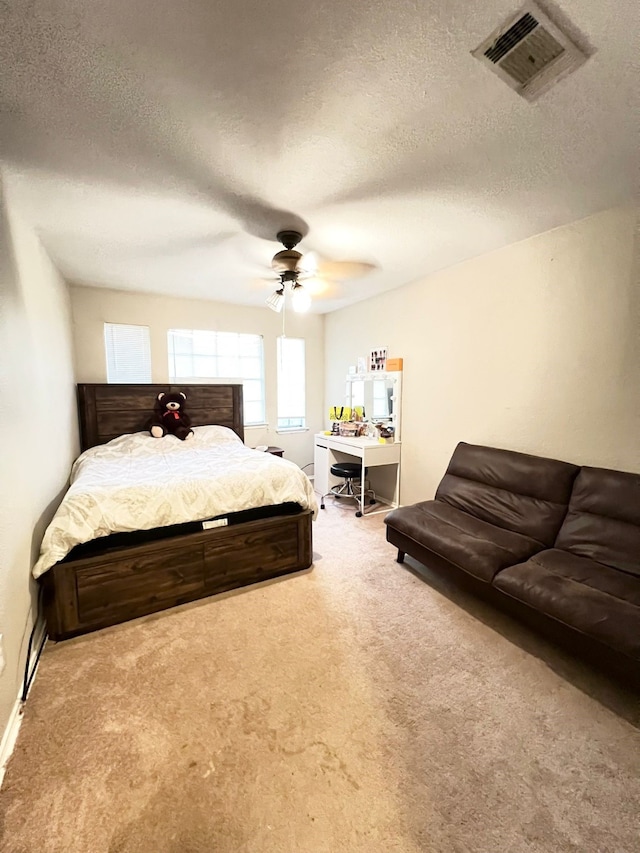 bedroom with ceiling fan, light colored carpet, and a textured ceiling