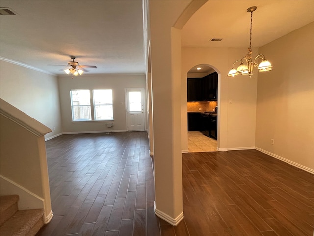 interior space featuring ornamental molding, ceiling fan with notable chandelier, and dark hardwood / wood-style flooring