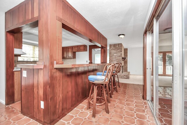 kitchen featuring a kitchen bar, kitchen peninsula, a textured ceiling, wooden walls, and range hood