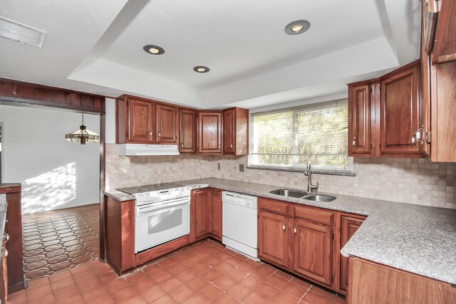 kitchen featuring sink, backsplash, a tray ceiling, white appliances, and pendant lighting