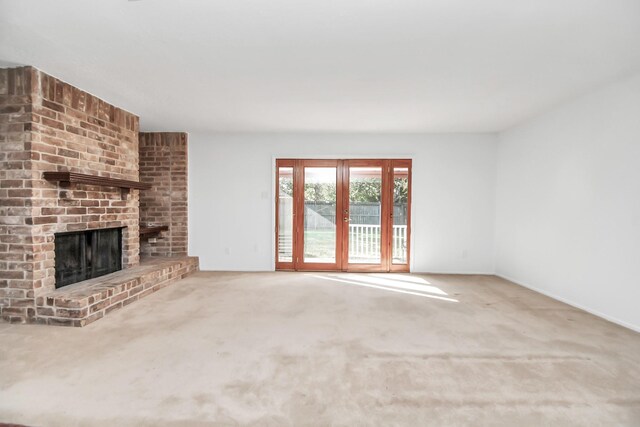 unfurnished living room featuring a brick fireplace, french doors, and carpet floors