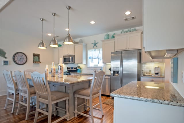 kitchen with wood-type flooring, white cabinetry, stainless steel appliances, a breakfast bar area, and light stone countertops