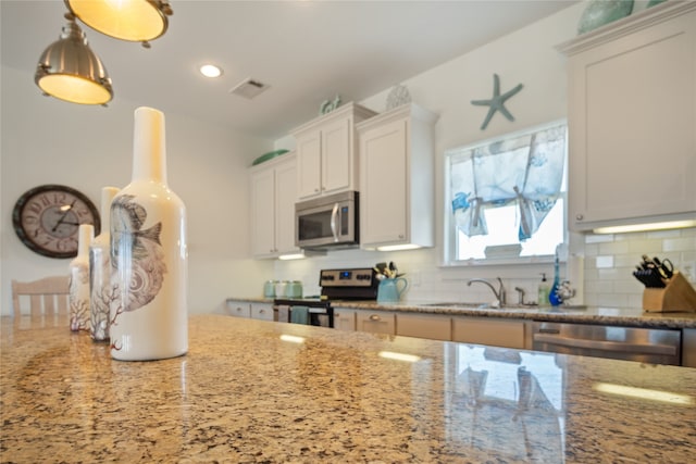 kitchen featuring hanging light fixtures, white cabinetry, light stone counters, tasteful backsplash, and stainless steel appliances