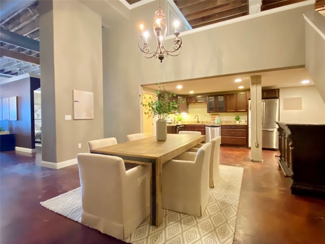 dining area with a notable chandelier, a towering ceiling, concrete floors, and sink