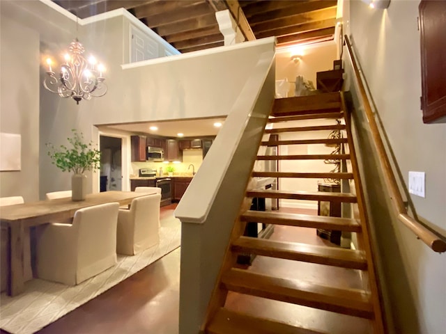 staircase featuring a towering ceiling, a chandelier, sink, and concrete flooring