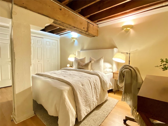 bedroom featuring light hardwood / wood-style floors, beamed ceiling, and a closet