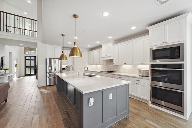 kitchen with pendant lighting, hardwood / wood-style flooring, sink, white cabinetry, and stainless steel appliances