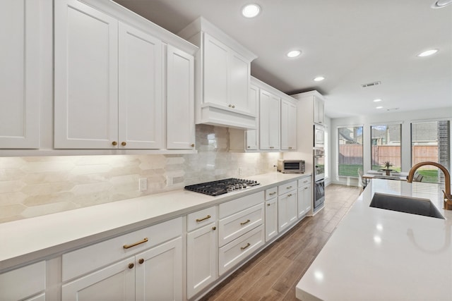 kitchen with stainless steel appliances, white cabinetry, wood-type flooring, and sink