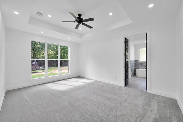 empty room with a tray ceiling, ceiling fan, light colored carpet, and a healthy amount of sunlight