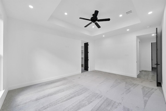 unfurnished room with ceiling fan, a raised ceiling, and light carpet