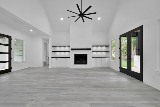 unfurnished living room with light wood-type flooring, high vaulted ceiling, and french doors