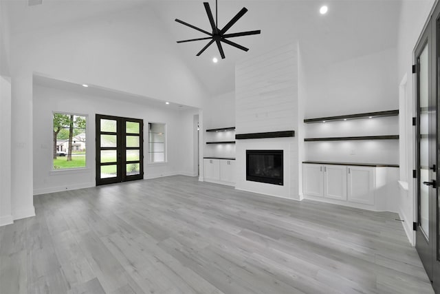 unfurnished living room with french doors, a large fireplace, ceiling fan, high vaulted ceiling, and light hardwood / wood-style floors