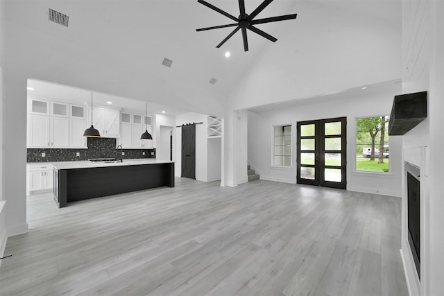 unfurnished living room featuring french doors, light hardwood / wood-style floors, high vaulted ceiling, and ceiling fan