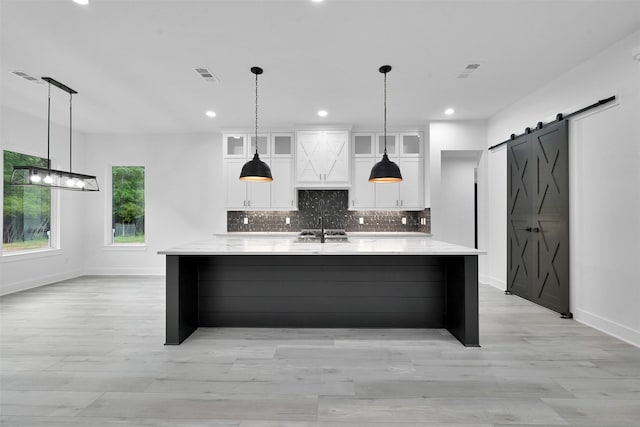 kitchen featuring white cabinets, a large island with sink, a barn door, and light stone countertops