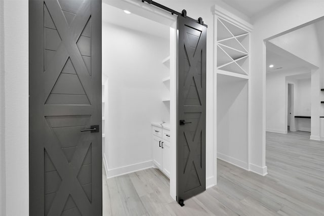 walk in closet with a barn door and light hardwood / wood-style flooring