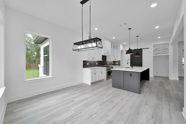 kitchen featuring white cabinets, a center island with sink, sink, high end stove, and decorative light fixtures