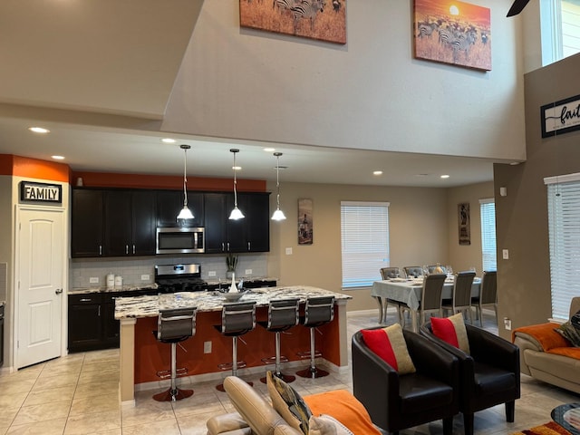 kitchen with stainless steel appliances, light stone counters, pendant lighting, a kitchen island with sink, and a breakfast bar