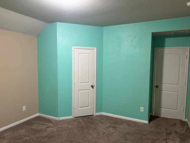 empty room with dark carpet, a textured ceiling, and vaulted ceiling