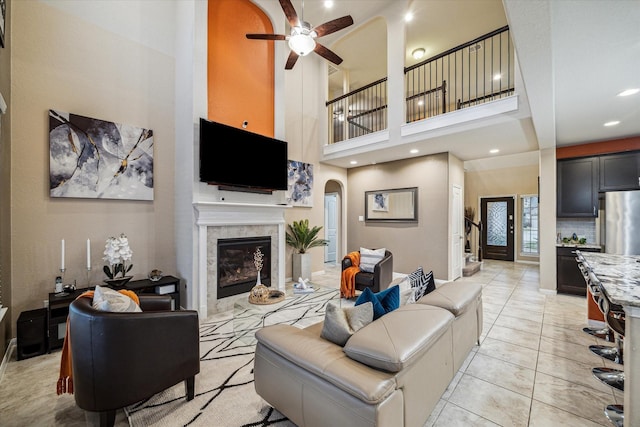 tiled living room featuring ceiling fan, a towering ceiling, and a fireplace