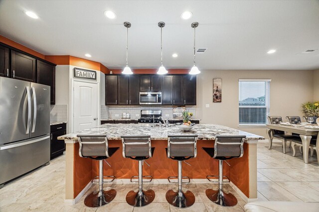 kitchen featuring a breakfast bar area, appliances with stainless steel finishes, pendant lighting, and a center island with sink